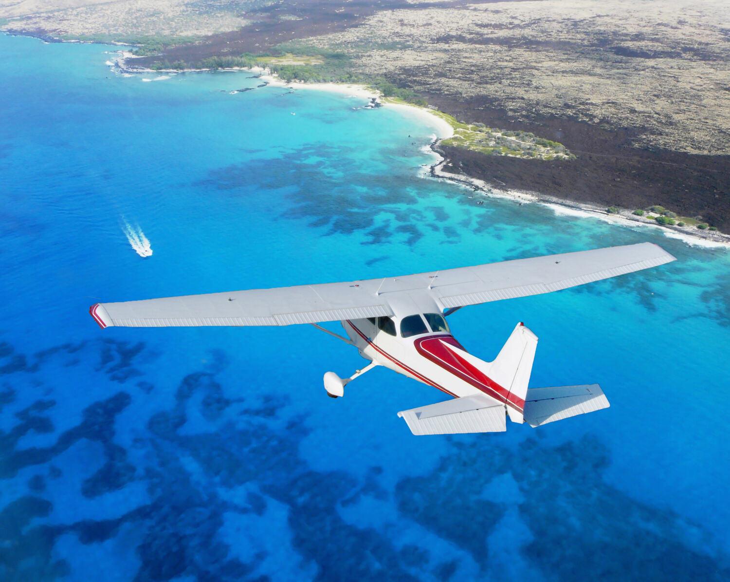 High-wing single-engine Cessna in cruise above a turquoise coastline