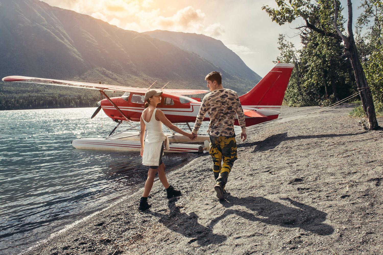 Two people walking toward a floatplane on a lakeshore beach